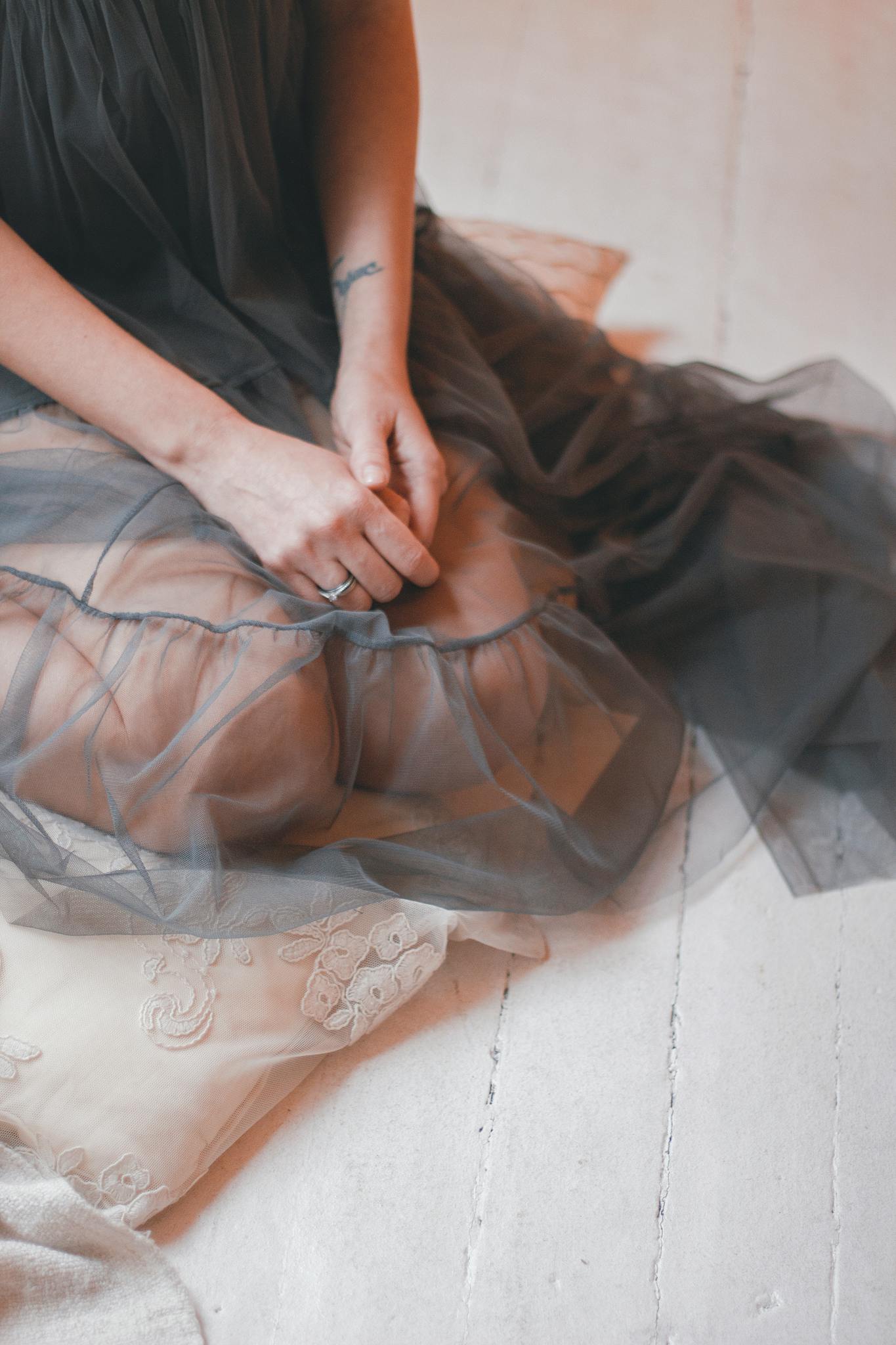 Woman in a sheer gray dress sitting gracefully on a wooden floor.